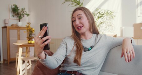 Web conference app. Happy attractive young blonde woman smiles using smartphone video call to talk...