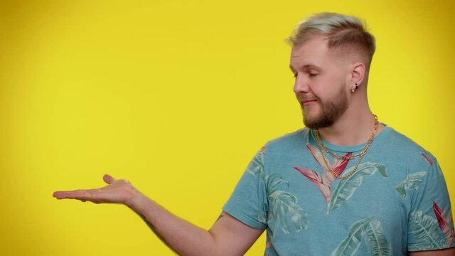 Handsome stylish bearded guy showing thumbs up and pointing empty place, advertising area for commercial text, copy space for goods promotion. Young adult man. Studio shot on yellow wall background