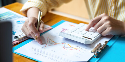 Close up Business woman using calculator and laptop for do math finance on wooden desk in office and business working background, tax, accounting, statistics and analytic research concept