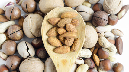 Nuts almonds close-up in a wooden spoon on the background of a scattering of different nuts. Assorted nuts