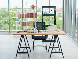 Scientist workplace in an open space. A wooden table near the windows with a cityscape view. There are laptop, microscope, stethoscope, dietary supplements on table with bookshelf in the background