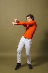 Tall handsome man dressed in orange turtleneck and white jeans posing on the green background