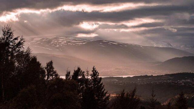 Sun rays shining through the clouds over the Mo i Rana town in Northern Norway. The thick cover of the blue-pink clouds hanging in the sky. Mountains covered with dense forest surround the valley