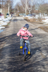Little girl learns to ride a two-wheeled bicycle on the road in the village