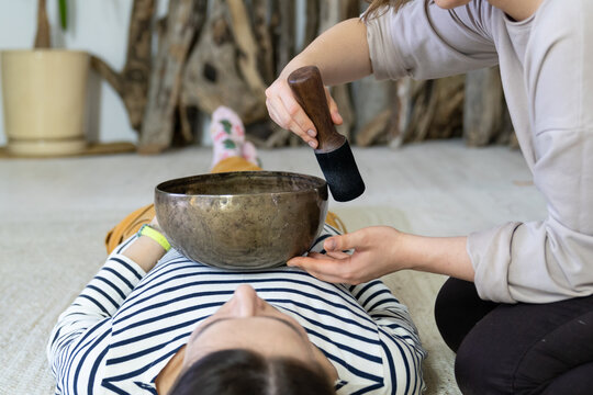 Young female having tibetan massage, singing bowl therapy with traditional tibet cymbals at home. Caucasian woman relax with alternative buddhism medicine. Wellbeing, wellness, stress relief concept