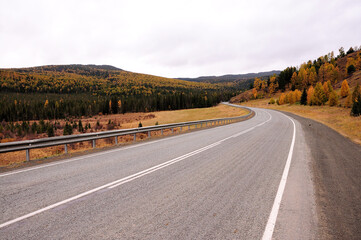 A turn of an asphalt road at the foot of a high hill in the autumn steppe.