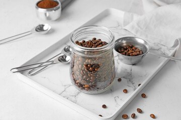 Jar and pot with coffee beans on light background