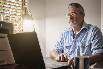 A senior man sitting at a desk in front of a laptop computer