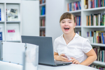 laughing girl with syndrome down uses a laptop at library. Education for disabled children concept