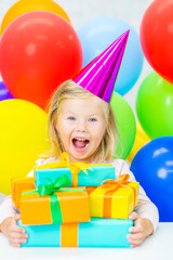 Obraz premium Happy little girl wearing party's cap holds many gift boxes