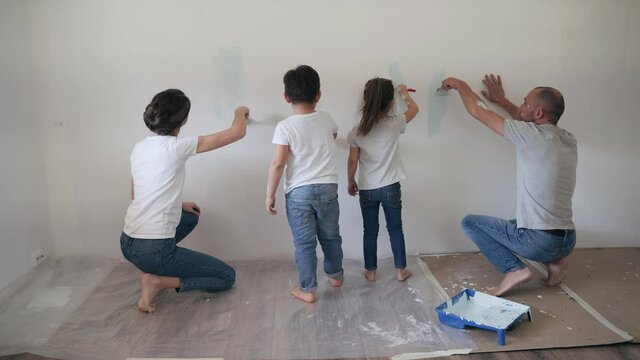 Caucasian family paints the wall with paint brushes Dad mom son and daughter together make repairs at home Parents teach their children to make repairs Funny kids Happy family