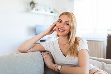 Smiling young woman relaxing while sitting on comfortable couch in living room. Weekend. Cheerful woman Sitting On Couch Relaxing At Home On Weekend Morning. Empty Space