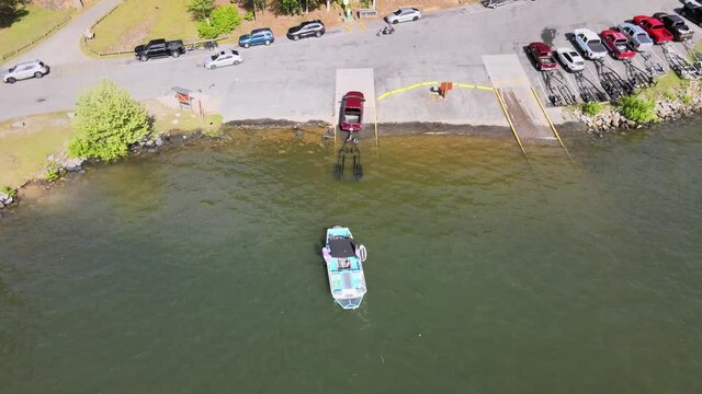 Wakeboard boat being loaded on a trailer at the boat ramp. Crowded lake weekend with several boat trailers lined up.
