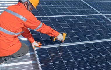 Technician with drill installing solar panels on roof.Male in protective helmet installing solar...