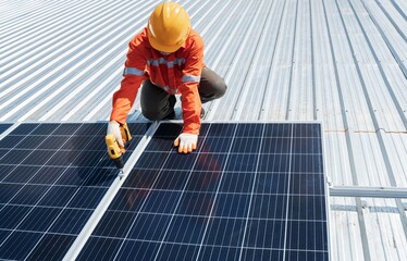 Technician with drill installing solar panels on roof.Male in protective helmet installing solar photovoltaic panel using screwdriver mounting solar module on roof. Alternative energy ecological.