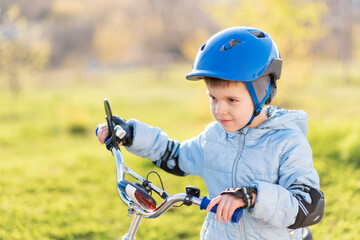 Fototapeta na wymiar A child in a helmet learns to ride a bike on a sunny day at sunset