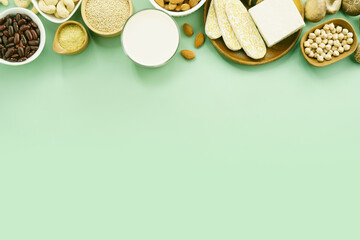 Top view of vegan sources of protein and B12, almonds, organic chickpeas, homemade tempeh, soy milk, nutritional yeast, quinoa and tofu beautiful arranging on green background with copy space.