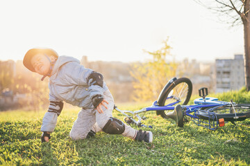 A small child in a helmet and protection fell from a bicycle onto the grass and was not injured