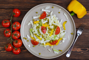fresh summer vegetable salad with peking cabbage, cherry tomatoes, green peas and yellow bell pepper on a ceramic plate