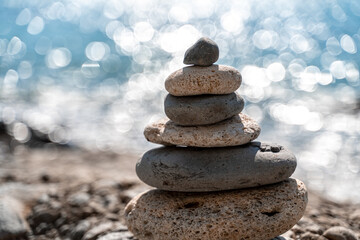 Fototapeta na wymiar Tower of stones. Balanced pebble pyramid on the beach on a sunny day. Blue sea on the background. Selective focus, bokeh. Zen stones on the sea beach, meditation, spa, harmony, tranquility, balance