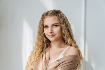 an attractive young woman with blonde hair and long curly hair. portrait of a beautiful girl in beige clothes with light natural hair