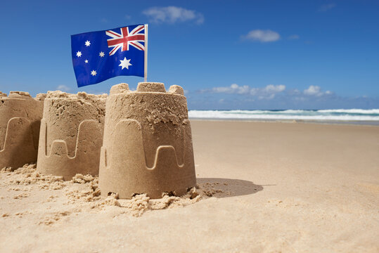 Australian flag on top of group of three sandcastles at the beach