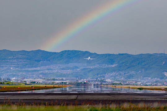 虹のかかる空へ向かって離陸しようとする飛行機の後ろ姿；大阪国際空港での飛行機離陸イメージ