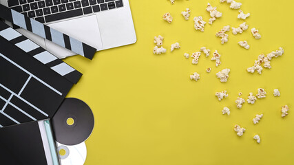 Computer laptop, clapboard and popcorn on yellow background.