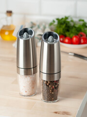 Electric spice mills made of metal. On a light wooden background. In the background is a plate with...