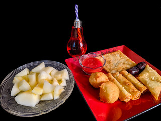 iftar food platter during the holy month of Ramadan with some melon slices and pakistani traditional drink on black backdrop