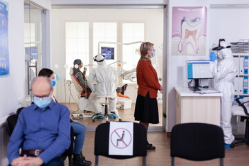 Dentist doctor in ppe suit consulting patient in dental clinic dressed in ppe suit as safety precation during global pandemic with coronaivurs. Senior woman talking with dentistiry stomatology