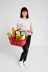 Obraz na płótnie Canvas young woman with shopping basket full of products over white background