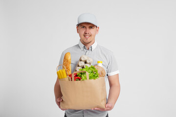 delivery man in uniform holding paper bag full of products over white background