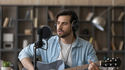 Close up man in headphones playing guitar, singing in microphone, popular musician artist recording...