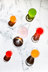Different glasses with bright color drinks, in direct hard light, long shadows, marble background
