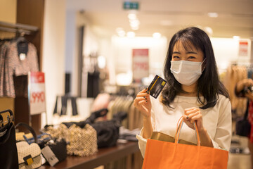 Asian young woman wearing medical mask and holding credit card at shopping mall