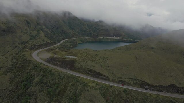 Mystic aerial view showing red car driving on road with fog between mountains and famous Atillo Lake in valley. Ecuador,