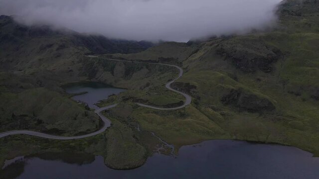 Aerial flyover serpentines between overgrown mountains near Atillo Lake in Ecuador. Dramatic atmosphere with cloudscape and mist.