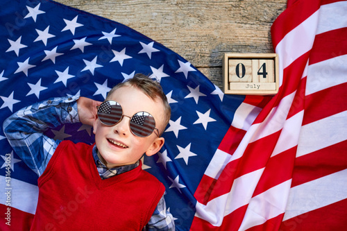 Cute and cheerful guy lying on a wooden background next to the American flag with glasses. Independence