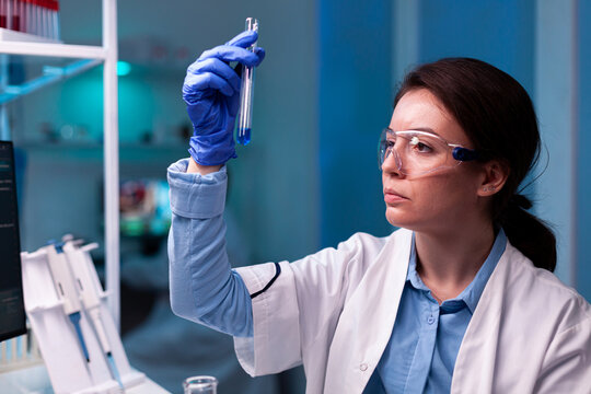 Scientist looking at testube with sample, analyzing liquid experiment. Pharmaceutical biotechnologist in research laboratory works with test tube to find vaccine glove.