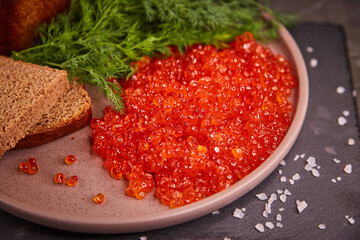 Delicious red caviar in a plate on the table, dark background. A beautiful and hearty dinner with red caviar. seafood and seafood delicacies