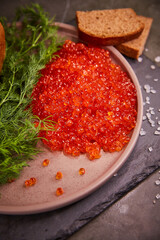 Delicious red caviar in a plate on the table, dark background. A beautiful and hearty dinner with red caviar. seafood and seafood delicacies