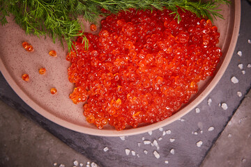 Delicious red caviar in a plate on the table, top view, dark background. A beautiful and rich dinner with red caviar. seafood and seafood delicacies