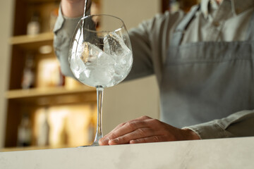 Bartender in the apron stirring an ice cubes in the cocktail glass on the background of bar