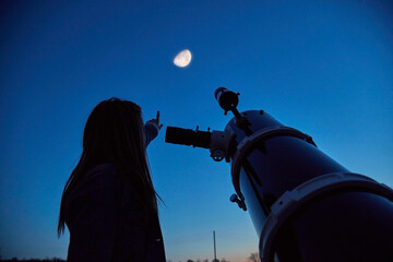 Woman looking at night sky with amateur astronomical telescope.