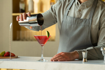 Bartender pouring Cosmopolitan cocktail in martini glass