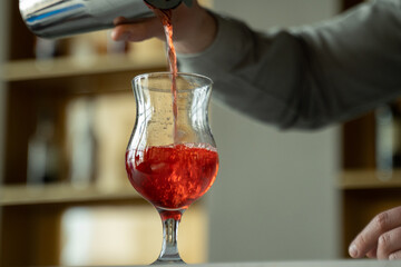 Close-up bartender professionally pours cocktail from shaker into glass. 
