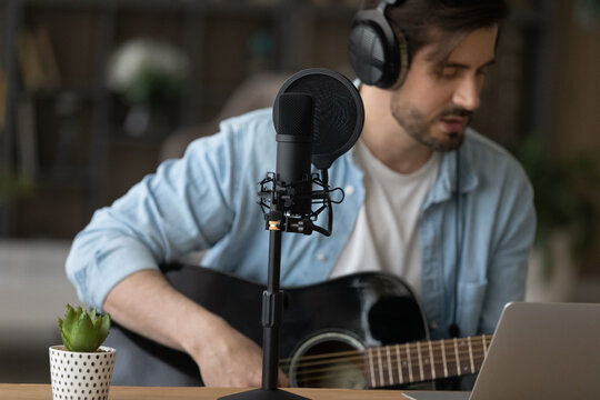 Close up cropped professional microphone, man in headphones playing acoustic guitar and singing, musician artist recording song, making music in home studio, using laptop, teacher shooting webinar - Powered by Adobe