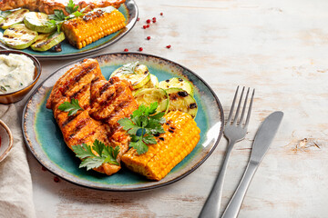 Grilled chicken breast with corn and zucchini on a blue plate top view. Summer dish with grilled chicken and vegetables on the white background 
