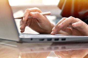 Woman hand typing on modern laptop with sunlight background.